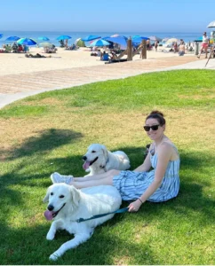 Woman sitting on grass with two dogs on a beach | 24th Street Dental Biltmore in Phoenix, AZ
